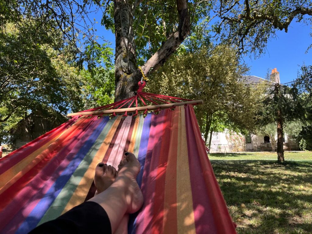 une femme se détend dans un des hamacs du jardin de la thébaïde on voit ses pieds