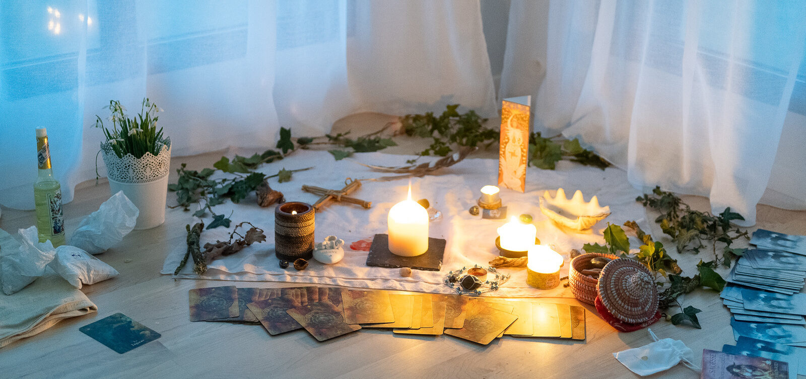 un autel de cérémonie du Sabbat de Imbolc est disposé au sol. on voit des bougies, des croix de Imbolc, des cartes d'oracle, des fleurs, des offrandes. L'image est douce et claire, l'ambiance est sereine